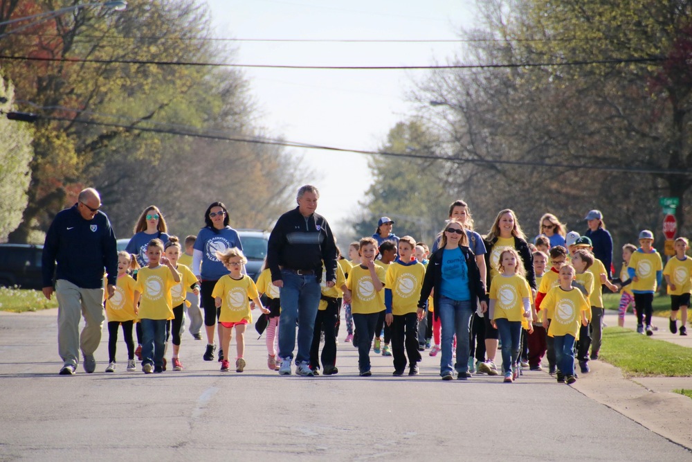 Superintendent Scott Olinger and School Board members Scott Flood and Jessica Elston (President), lead first grade students down Buchanan Street in the final stretch of the Walkathon.
