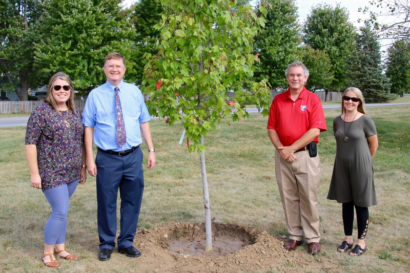 Katie Chamness, Scott Flood and Jessica Elston of the Plainfield School Board, pose with Brad DeHoff in front of his newly planted tree of honor.