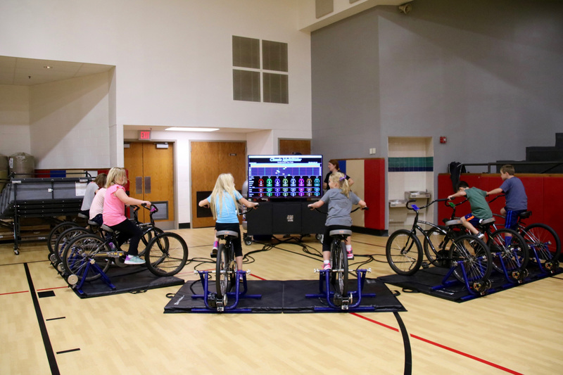 On stationary bikes, students ride different courses requiring varying degrees of exertion. A massive monitor helps them chart their progress.