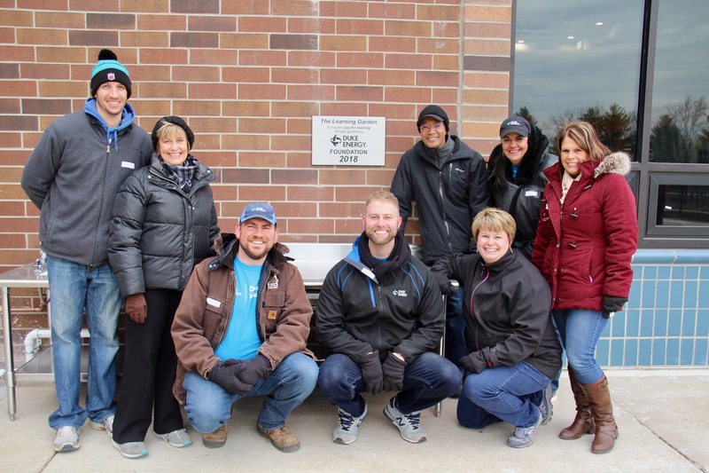 Duke Energy volunteers, along with Dr. Giesting, pose in front of the sign thanking Duke Energy for their sponsorship of the Learning Garden. 