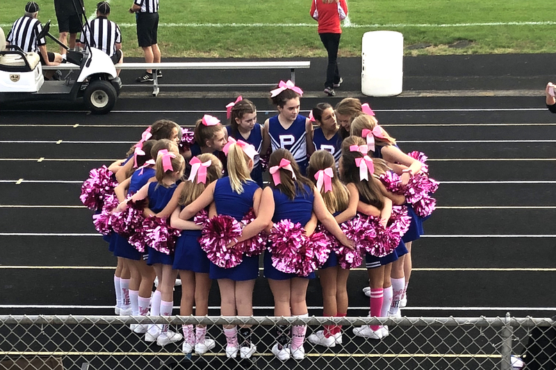 8th grade cheerleaders huddle with their pink pom pons, borrowed from the PHS squad