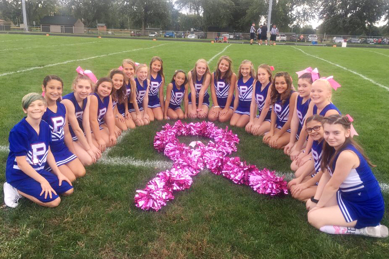 8th grade cheerleaders surround the signature pink ribbon that represents breast cancer.